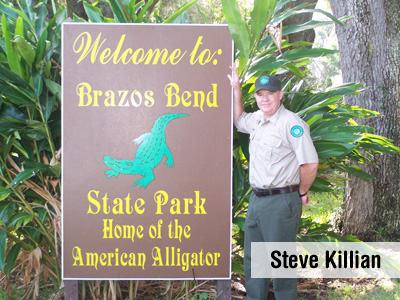 Steve poses next to a park sign labelled: Welcome to Brazos Bend State Park, home of the American Alligator